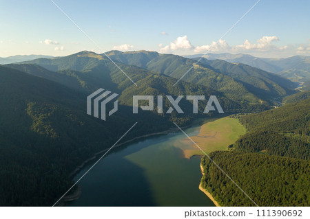 Aerial view of big lake with clear blue water between high mountain hills covered with dense evergreen forest. Aerial view of big lake with clear blue water between high mountain hills covered with dense evergreen forest. 111390692
