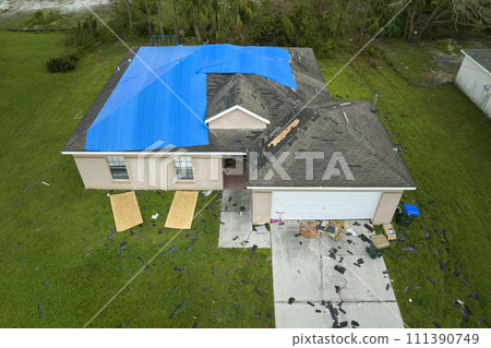 Top view of leaking house roof covered with protective tarp sheets against rain water leaks until replacement of asphalt shingles. Damage of building rooftop as aftermath of hurricane Ian in Florida 111390749
