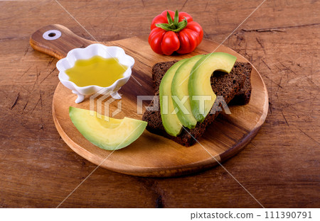 Olive oil, tomato, bread with avocado on wood cutting board. Olive oil, tomato, bread with avocado on wood cutting board. 111390791