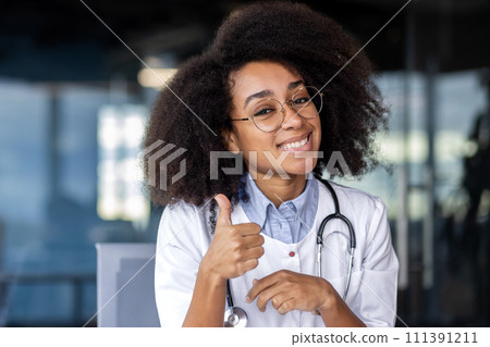 A female doctor with black hair and glasses is happily smiling, showing a thumbs up gesture, at a vision care event. A female doctor with black hair and glasses is happily smiling, showing a thumbs up gesture, at a vision care event. 111391211