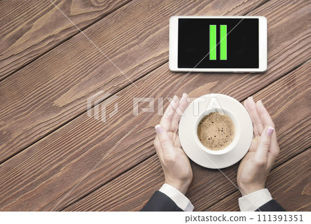 Coffee break. Female hands in business suit touches a cup of coffee and a pause icon on a phone screen next to it, copy space. Coffee break. Female hands in business suit touches a cup of coffee and a pause icon on a phone screen next to it, copy space. 111391351