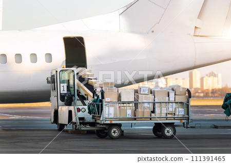 Close-up detail view of cargo cart trolley full with commercial parcels against turboprop cargo plane. Air mail shipping and logistics. Import export operations. Commercial charter flight service 111391465