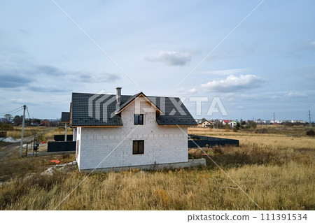 Aerial view of unfinished house with aerated lightweight concrete walls and wooden roof frame covered with metallic tiles under construction 111391534