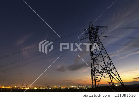 Transmission and long distance distribution of electricity concept. High voltage tower with electric power lines stretching on dark blue starry sky.and bright distant city lights background. 111391536