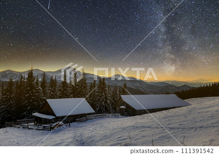 Old wooden house, hut and barn, pile of firewood in deep snow on mountain valley, spruce forest, woody hills on dark starry sky and Milky Way copy space background. Mountain winter night landscape. Old wooden house, hut and barn, pile of firewood in deep snow on mountain valley, spruce forest, woody hills on dark starry sky and Milky Way copy space background. Mountain winter night landscape. 111391542