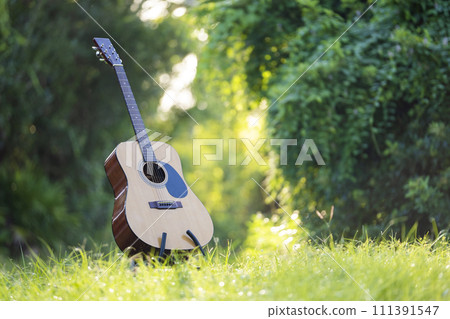 Acoustic guitar outdoors on greenery background. Concept of calm music Acoustic guitar outdoors on greenery background. Concept of calm music 111391547