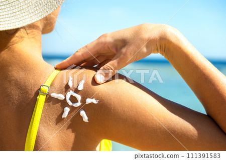 Back view of young woman tanning at the beach with sunscreen cream in sun shape on her shoulder. UV sunburn protection and sunblock skincare concept 111391583