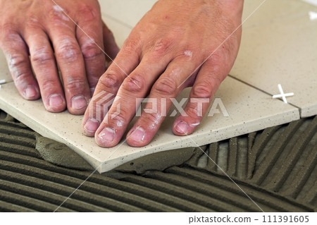 Ceramic tiles and tools for tiler. Worker hand installing floor tiles. Home improvement, renovation - ceramic tile floor adhesive, mortar. 111391605