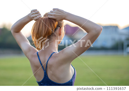 Closeup of yong sportive woman with red hair standing outdoors with raised arms enjoying sunrise before training. Closeup of yong sportive woman with red hair standing outdoors with raised arms enjoying sunrise before training. 111391637