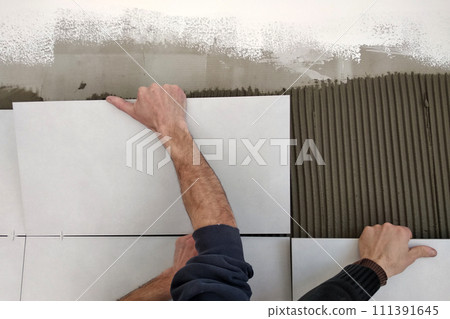 Worker hands putting ceramic tiles on the wall. Worker hands putting ceramic tiles on the wall. 111391645