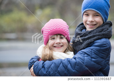 Two children boy and girl hugging each other outdoors wearing warm clothes in cold autumn or winter weather. Two children boy and girl hugging each other outdoors wearing warm clothes in cold autumn or winter weather. 111391687