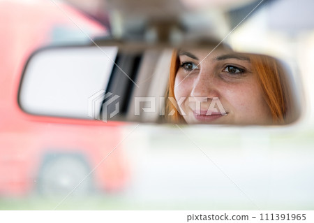 Young woman driver checking rear view mirror looking backwards while driving a car. 111391965