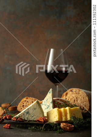 Cheese, bread, red wine, and walnuts on a stone table. 111392302