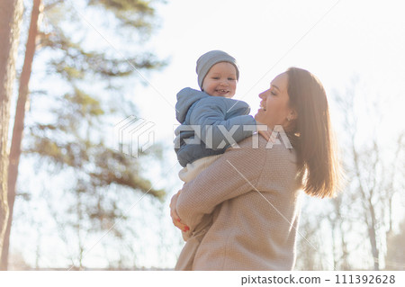 Happy family outdoor. Mother embracing her child outdoor. Mom lifting in air little toddler child son. Woman and little baby boy resting walking in park. Mother hugs baby with love care 111392628