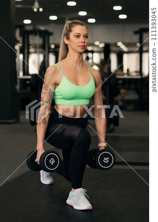Young woman does dumbbell lunges in gym 111393045