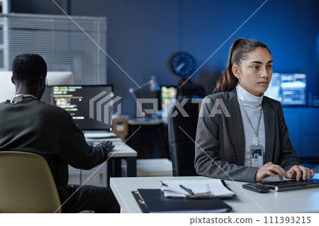 Portrait of young woman using computer in formal IT company office with blue neon light copy space Portrait of young woman using computer in formal IT company office with blue neon light copy space 111393215
