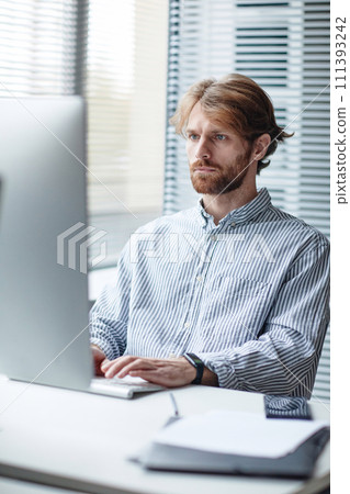 Graphic vertical portrait of bearded adult man using computer at workplace in IT office against window 111393242