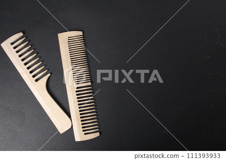Hairdresser's tools. Two wooden combs lie on a black background with space for copyspace text. Natural Comb Hairdresser's tools. Two wooden combs lie on a black background with space for copyspace text. Natural Comb 111393933