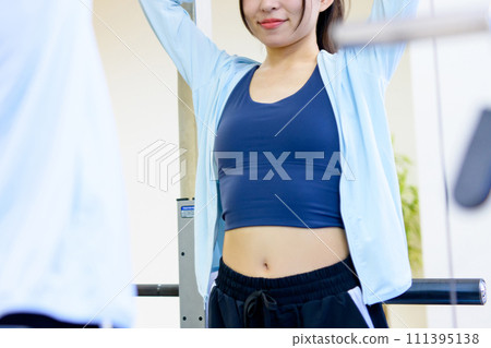 Young woman preparing to check her figure in the mirror at the gym, muscle training girl, tying her hair, faceless trimmed up 111395138