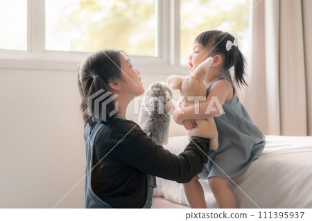 Elder asian sister and younger Asian sister playing animal hand puppet doll toys, sitting on bed, Educational preschool games, Having fun with kid at home concept.; Elder asian sister and younger Asian sister playing animal hand puppet doll toys, sitting on bed, Educational preschool games, Having fun with kid at home concept.; 111395937