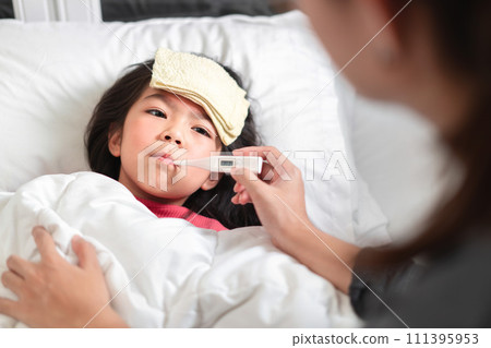 Asian mother measuring temperature girl with digital thermometer in her mouth on bed at morning time, Sick child have cool towel for reduce high fever, Selective focus, Healthy and infection concept Asian mother measuring temperature girl with digital thermometer in her mouth on bed at morning time, Sick child have cool towel for reduce high fever, Selective focus, Healthy and infection concept 111395953