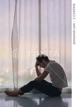 Depressed caucasian man losing job and heartbroken at same time sitting alone near window in dark at evening time with low light environment, PTSD Mental health and depression concept. 111395956