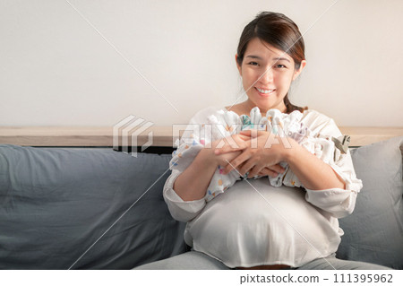 Pregnant asian woman smiling and hugging baby clothes for planning new born baby, Prepare before Give birth baby concept. Pregnant asian woman smiling and hugging baby clothes for planning new born baby, Prepare before Give birth baby concept. 111395962