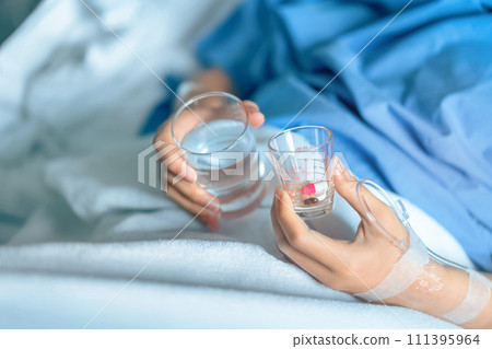 Asian woman patient with medical drip or IV drip holding water with medicine in hospital ward, Selective focus, Healthcare concept. Asian woman patient with medical drip or IV drip holding water with medicine in hospital ward, Selective focus, Healthcare concept. 111395964