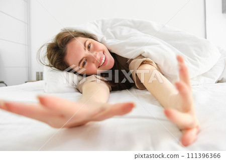 Cheerful girl stretching her arms in bed, waking up from good sleep or nap, enjoying the morning 111396366