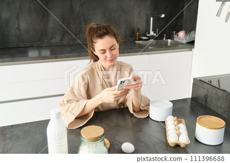 Attractive young cheerful girl baking at the kitchen, making dough, holding recipe book, having ideas 111396688