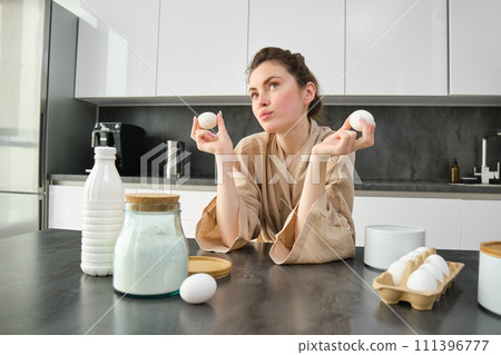 Attractive young cheerful girl baking at the kitchen, making dough, holding recipe book, having ideas 111396777