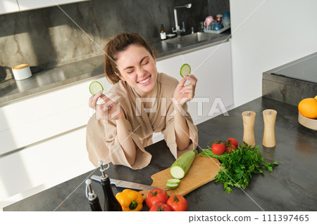 Portrait of beautiful brunette woman in the kitchen, wearing bathrobe, chopping vegetables on board, cooking healthy vegetarian food, preparing salad, making a meal Portrait of beautiful brunette woman in the kitchen, wearing bathrobe, chopping vegetables on board, cooking healthy vegetarian food, preparing salad, making a meal 111397465