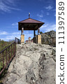 A gazebo with a bell on a rock, against the backdrop of the Shaonin Temple. View from the south. Village named after Kosta Khetagurov, Karachay district. Karachay-Cherkessia. Russia 111397589