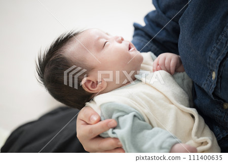 Image of a baby in baby clothes sleeping in his mother's arms, upper body on his back Image of a baby in baby clothes sleeping in his mother's arms, upper body on his back 111400635