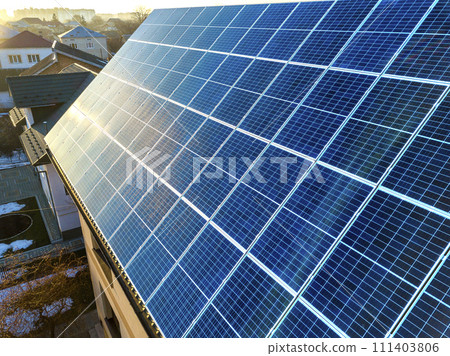 Close-up surface of lit by sun blue shiny solar photo voltaic panels system on building roof. Renewable ecological green energy production concept. Close-up surface of lit by sun blue shiny solar photo voltaic panels system on building roof. Renewable ecological green energy production concept. 111403806