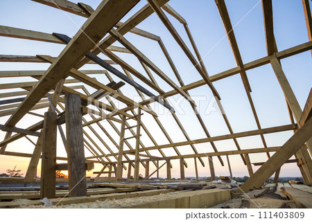 New wooden house under construction. Close-up of attic roof frame against clear sky from inside. Ecological dream home of natural materials. Building, construction and renovation concept. New wooden house under construction. Close-up of attic roof frame against clear sky from inside. Ecological dream home of natural materials. Building, construction and renovation concept. 111403809