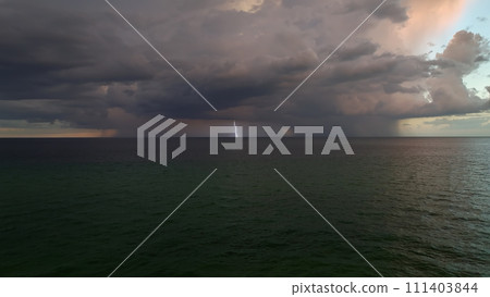 Dark stormy clouds forming on gloomy sky during heavy rainfall season over sea surface in evening Dark stormy clouds forming on gloomy sky during heavy rainfall season over sea surface in evening 111403844