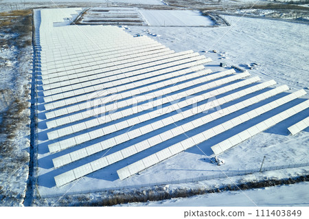Aerial view of snow covered sustainable electric power plant with rows of solar photovoltaic panels for producing clean electrical energy. Low effectivity of renewable electricity in northern winter Aerial view of snow covered sustainable electric power plant with rows of solar photovoltaic panels for producing clean electrical energy. Low effectivity of renewable electricity in northern winter 111403849
