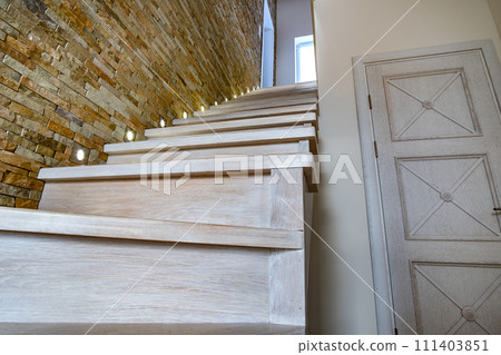 Stylish wooden contemporary staircase inside loft house interior. Modern hallway with decorative limestone brick walls and white oak stairs. Stylish wooden contemporary staircase inside loft house interior. Modern hallway with decorative limestone brick walls and white oak stairs. 111403851