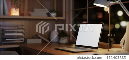 Modern and cozy home office workspace at night with a white-screen laptop computer on a wood table. 111403885