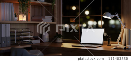 A modern, vintage, and cozy home office workspace at night with a white-screen laptop mockup. 111403886