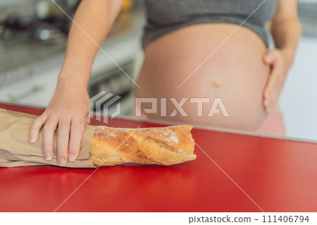 Pregnant woman eating bread in the kitchen. Exploring the impact of gluten during pregnancy: understanding the potential benefits and risks for maternal health and fetal development 111406794