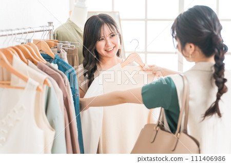 A woman and a shop clerk shopping for clothes at an apparel shop A woman and a shop clerk shopping for clothes at an apparel shop 111406986