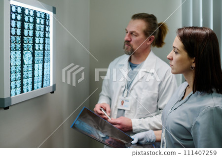 Doctors looking at brain scan on wall Doctors looking at brain scan on wall 111407259