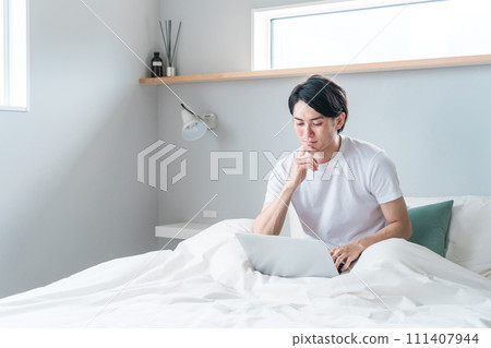 A young man using a laptop at home/hotel bedroom/bedroom (full remote/work from home/news) 111407944