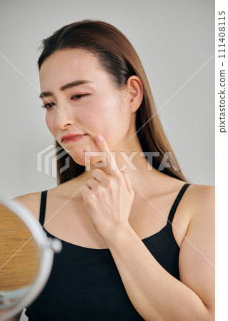 A woman in her 30s worries about wrinkles on her skin while looking in the mirror A woman in her 30s worries about wrinkles on her skin while looking in the mirror 111408115