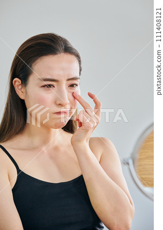 A woman in her 30s worries about wrinkles around her eyes while looking in the mirror. 111408121