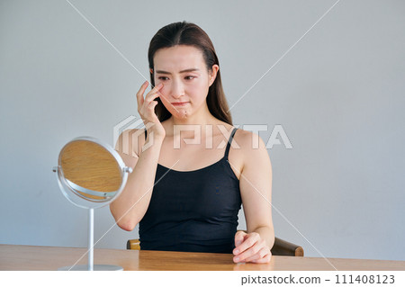 一位30多歲的女性在照鏡子時擔心眼睛周圍的皺紋。 一位30多歲的女性在照鏡子時擔心眼睛周圍的皺紋。 111408123