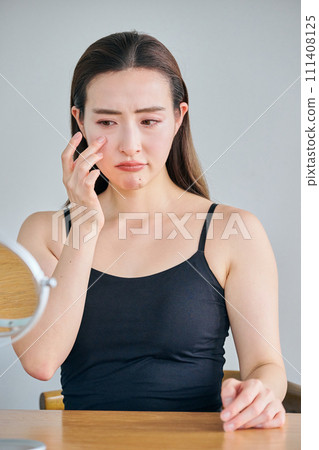 A woman in her 30s worries about wrinkles around her eyes while looking in the mirror. A woman in her 30s worries about wrinkles around her eyes while looking in the mirror. 111408125