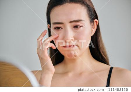 一位30多歲的女性在照鏡子時擔心眼睛周圍的皺紋。 111408126